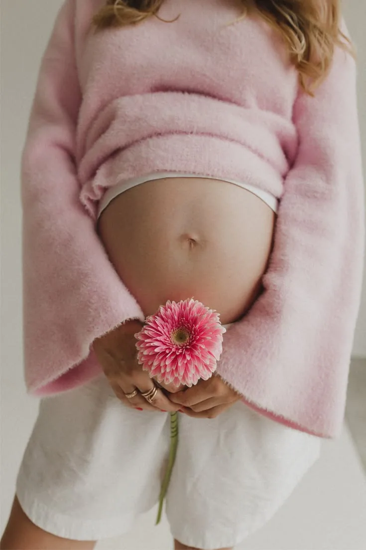 Gestante segurando uma gérbera rosa diante da barriga