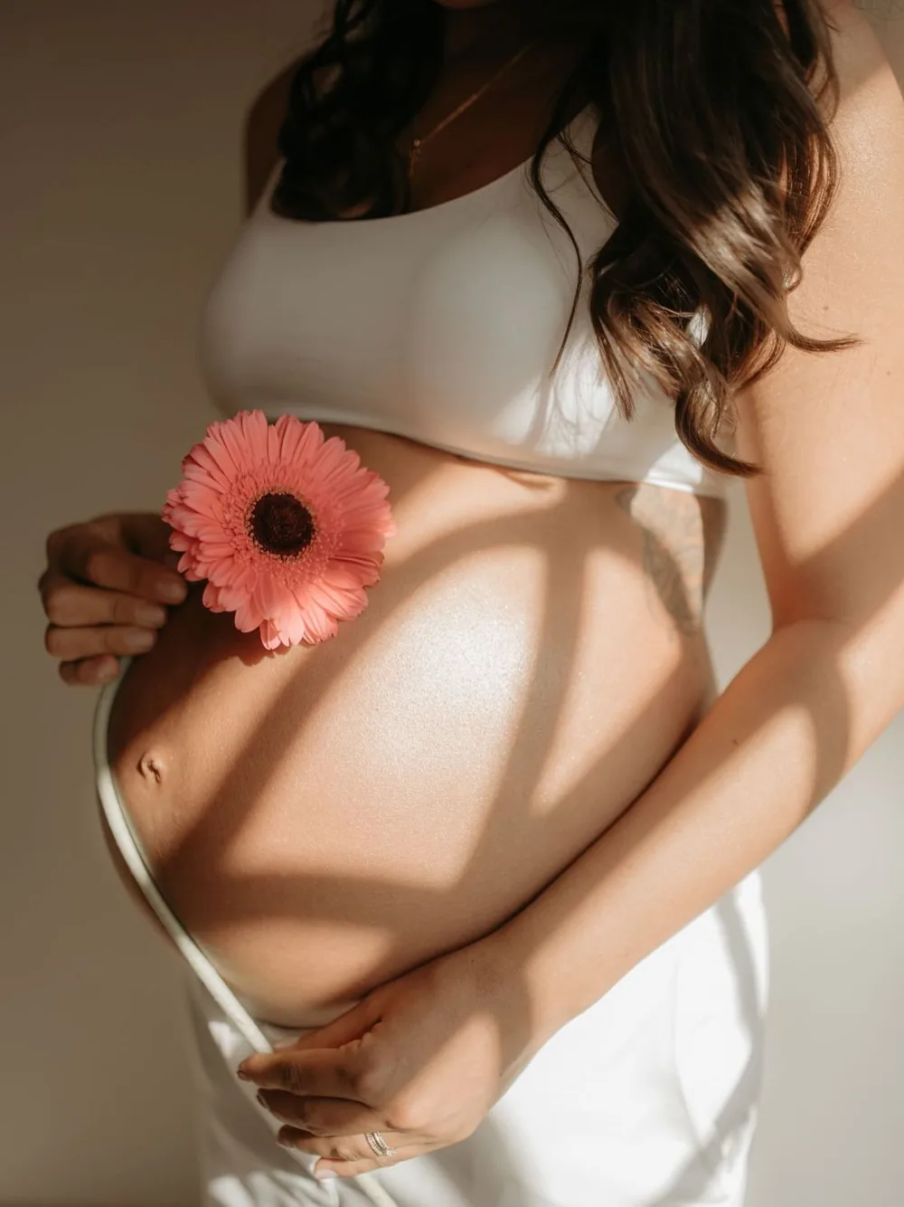 Gestante com uma gérbera rosa sobre a barriga, em luz natural